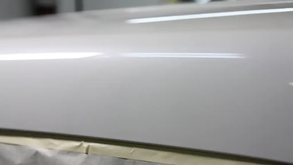 Close view of a white refinished panel with a long booth-light reflection running along its surface